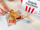 A person dipping a KFC chicken tender into a sauce container at KFC.
