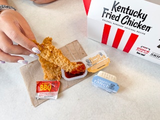 A person dipping a KFC chicken tender into a sauce container at KFC.