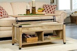 Lifestyle image of the oak Sauder Carson Forge Lift-Top Coffee Table in front of couch