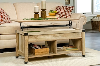 Lifestyle image of the oak Sauder Carson Forge Lift-Top Coffee Table in front of couch
