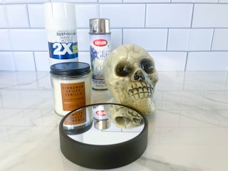 a plastic skull, mirrored candle holder, candle, and spray paint sitting on the counter ready for a diy project