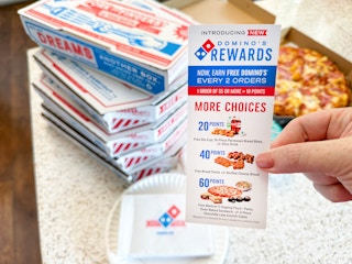 a dominos rewards flyer being held in front of pizza boxes