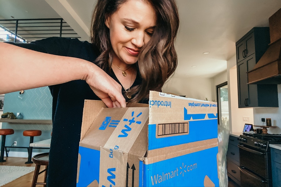 A woman opening a Walmart+ box in her kitchen.