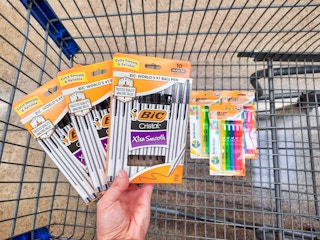 Three packages of BIC Cristal Pens held over Walmart shopping cart. The shopping cart has three package of BIC highlighters in it.