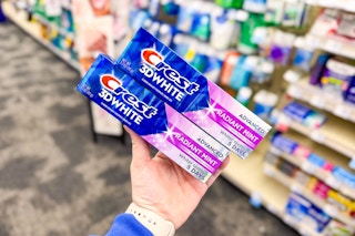person holding 2 crest 3d white toothpastes in an aisle