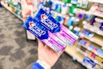 hand holding two tubes of crest toothpaste in a store aisle