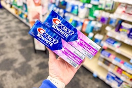 hand holding two tubes of crest toothpaste in a store aisle