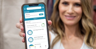 A woman holding up a cell phone displaying the Swagbucks app home screen