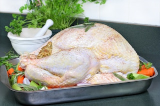 A Thanksgiving turkey in a pan on top of quartered vegetables.