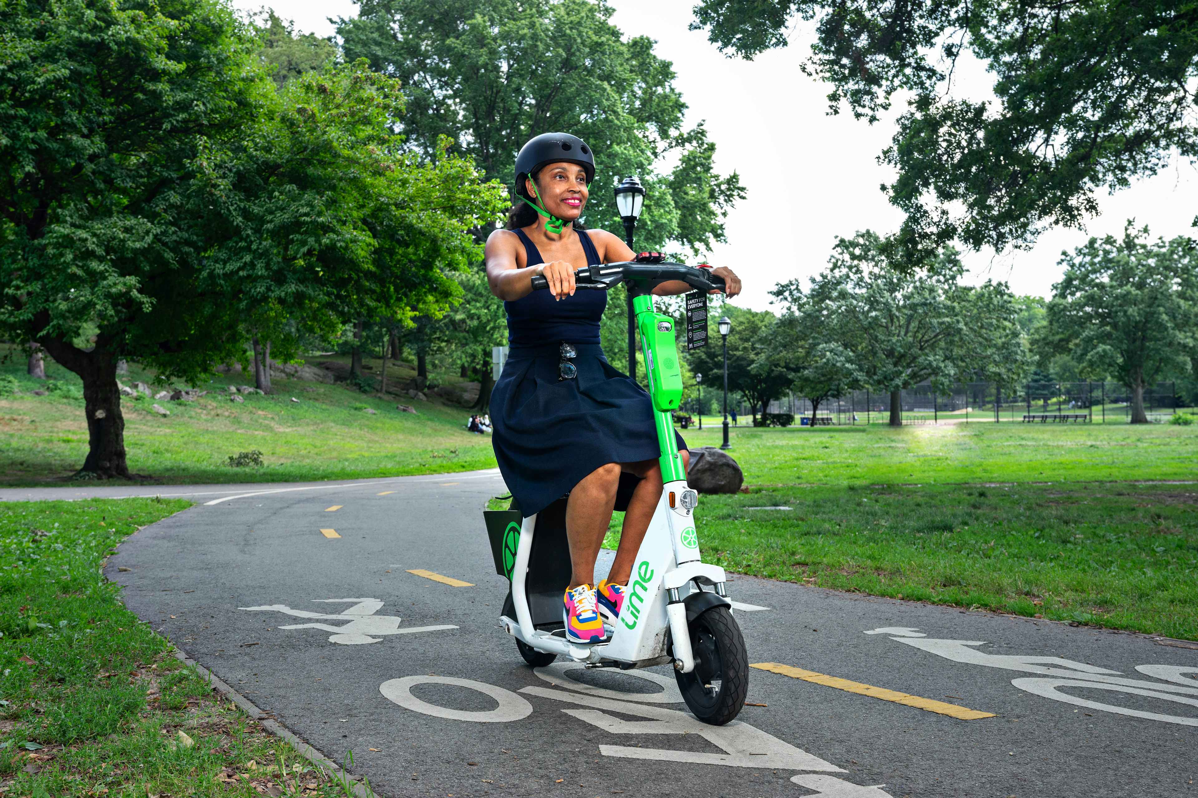 Person riding a seated lime scooter with a helmet on at a park