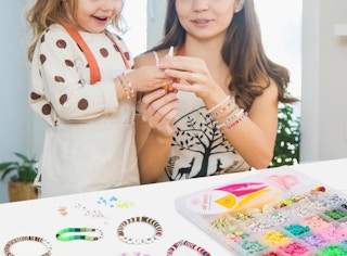 a mom and daughter making bracelets at a table with colorful clay beads