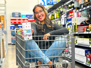 Lady in shopping cart showing KCL app 1-Clip deals on a phone