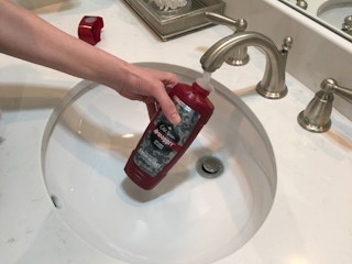 Person adding water to a bottle of old spice body wash.