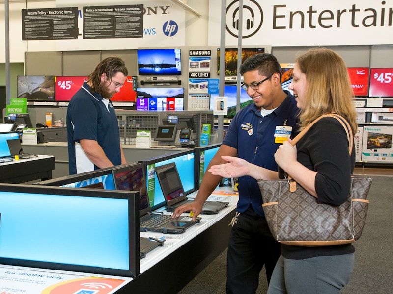 A Walmart employee talking to a customer in the electronics department