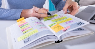 A person writing in a planner with many things scheduled for the week