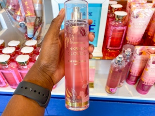 a person holding a body mist spray in front of a display in bath and body works