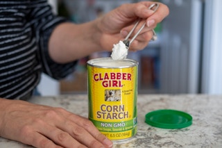 A person using a measuring spoon to scoop out corn starch from a canister