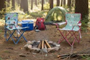 dinosaur and unicorn themed kids' folding chairs in a wooded area with a tent and other camping gear in the background