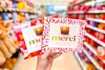 person holding 2 boxes of merci chocolates