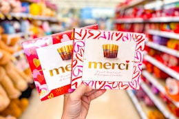 person holding 2 boxes of merci chocolates