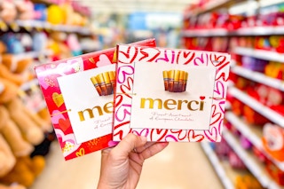 person holding 2 boxes of merci chocolates