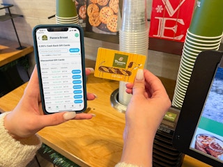 A cell phone displaying Raise.com held next to a gift card at the Panera self checkout