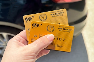 Someone holding two AAA Membership cards in front of a car