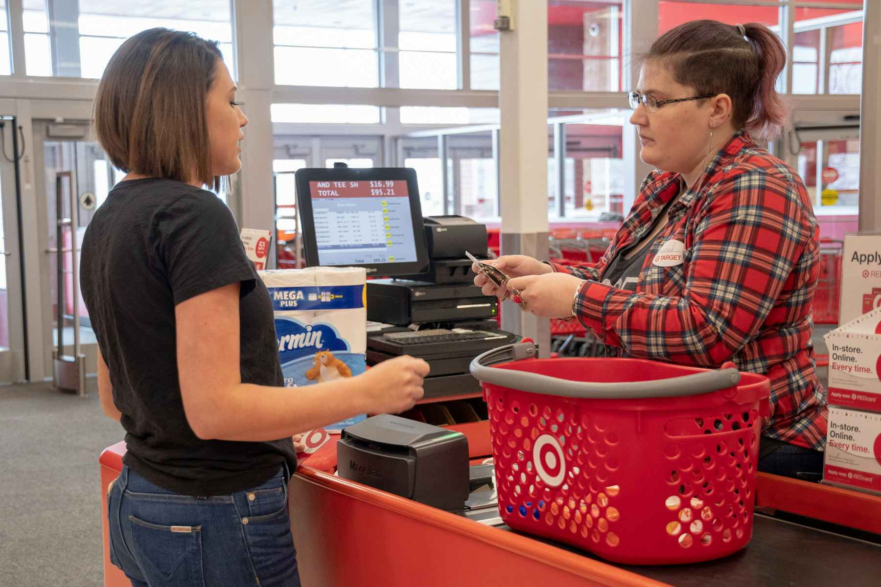 A woman standing at Target checkout with a basket on the conveyer belt and a cashier scanning her items.