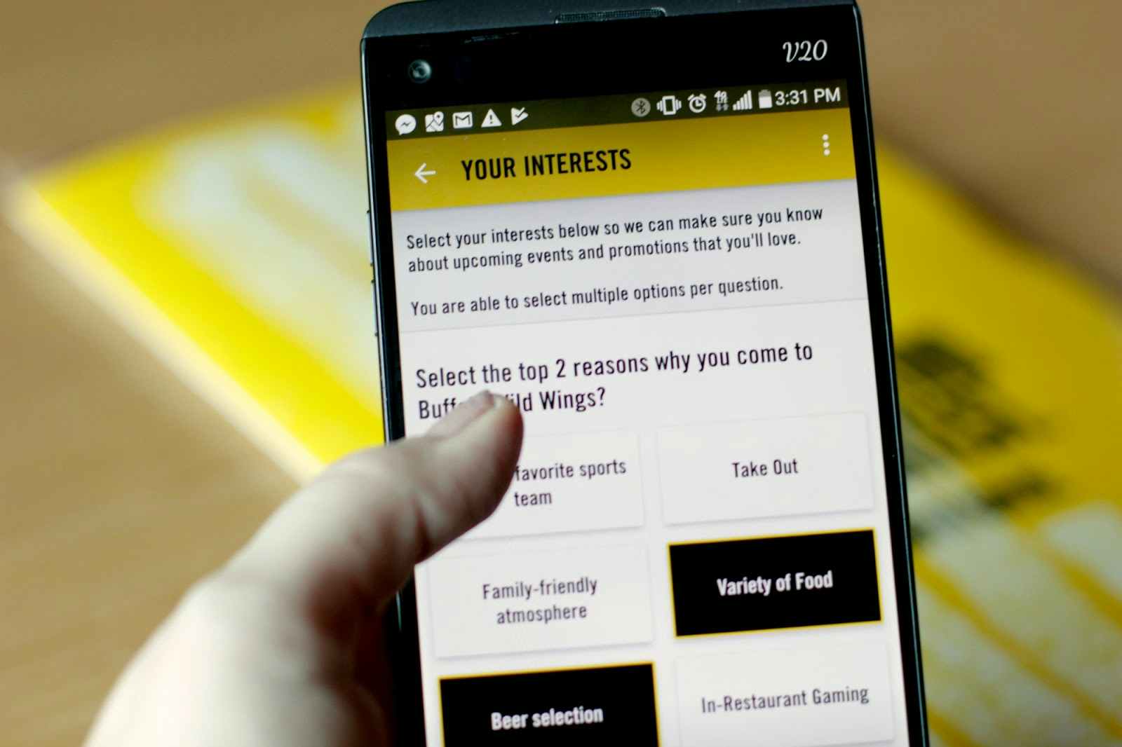 A person holding their phone center-frame with the Buffalo Wild Wings app open to a survey used to gauge the user's interests. The survey...