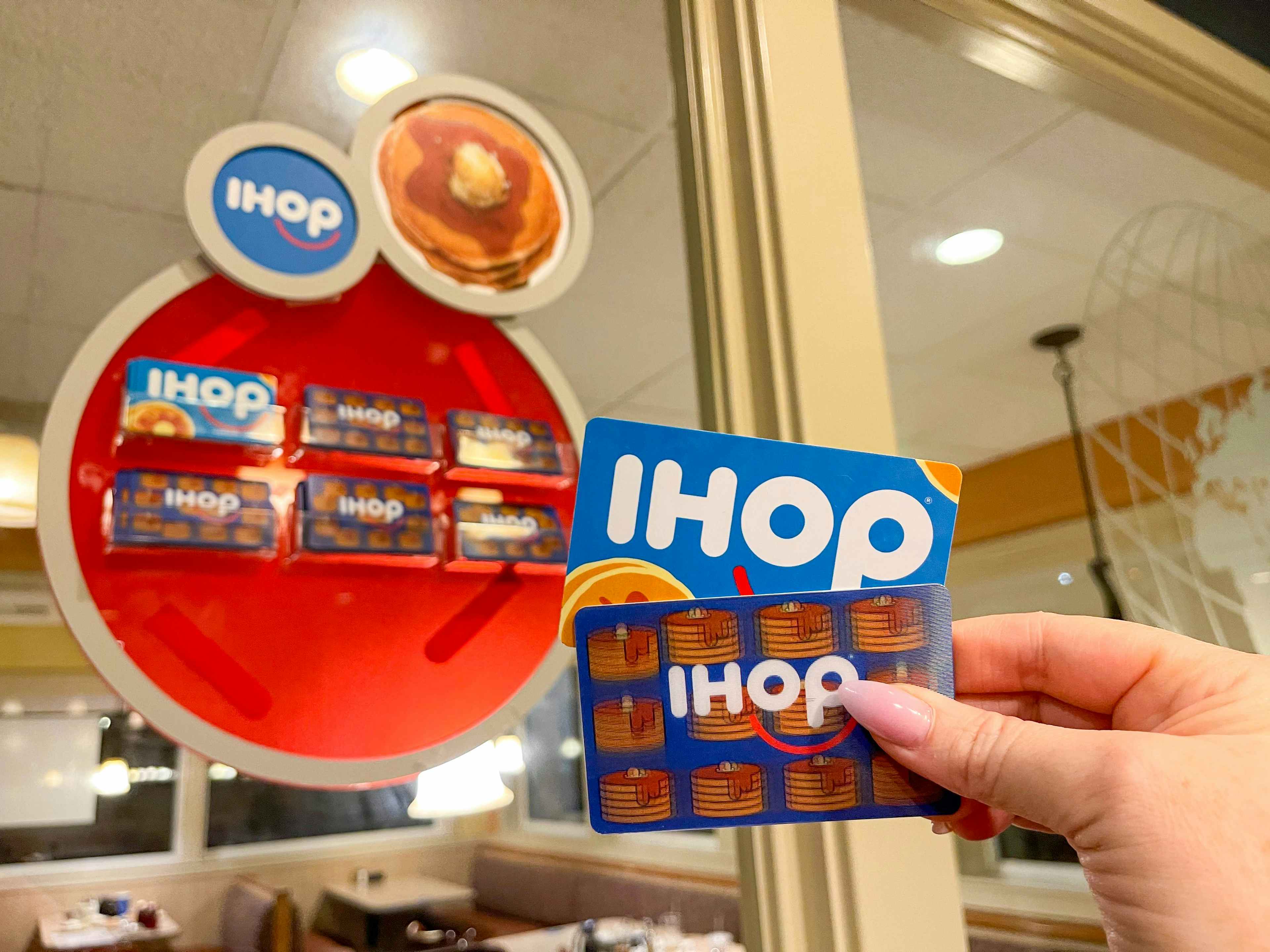 someone holding up two IHOP gift cards inside an IHOP restaurant