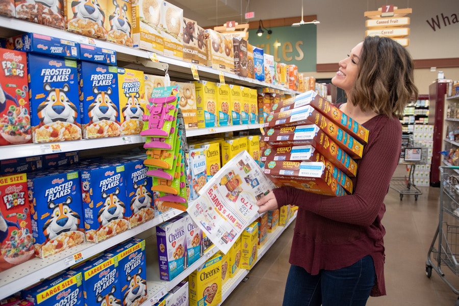 A woman holding multiple boxes of cereal in her arms while standing in the cereal aisle.