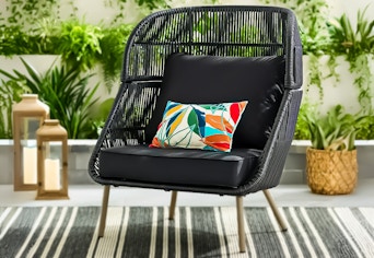 Lifestyle image of the Better Homes & Gardens Tarren Wicker Accent Chair in black set up outdoors