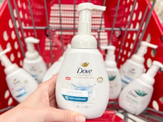 A Dove hand soap held out by hand in front of several other Dove hand soaps sitting in a store cart.
