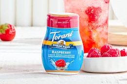 Lifestyle image of the Torani Sugar Free Raspberry Liquid Drink Enhancer next to a bowl of raspberries and a beverage