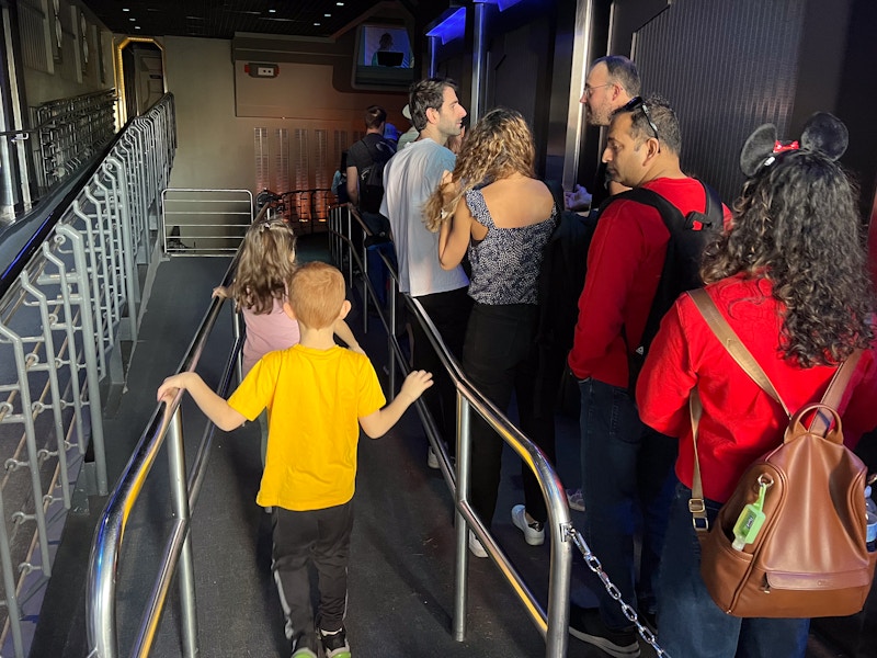 two children walking down an empty lane next to a long line at disney world