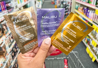 hand holding three Malibu C hair satchets in aisle