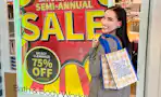 a woman standing next to a Bath and Body Works Semi-Annual Sale sign holding a shopping bag