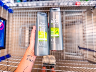 hand holding two bottles of dove men care 2-in-1 shampoo over walmart cart