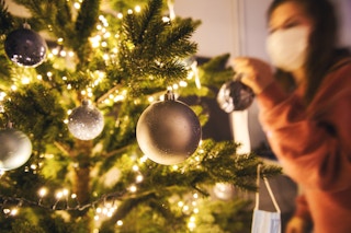 A woman wearing a mask, decorating a Christmas tree.