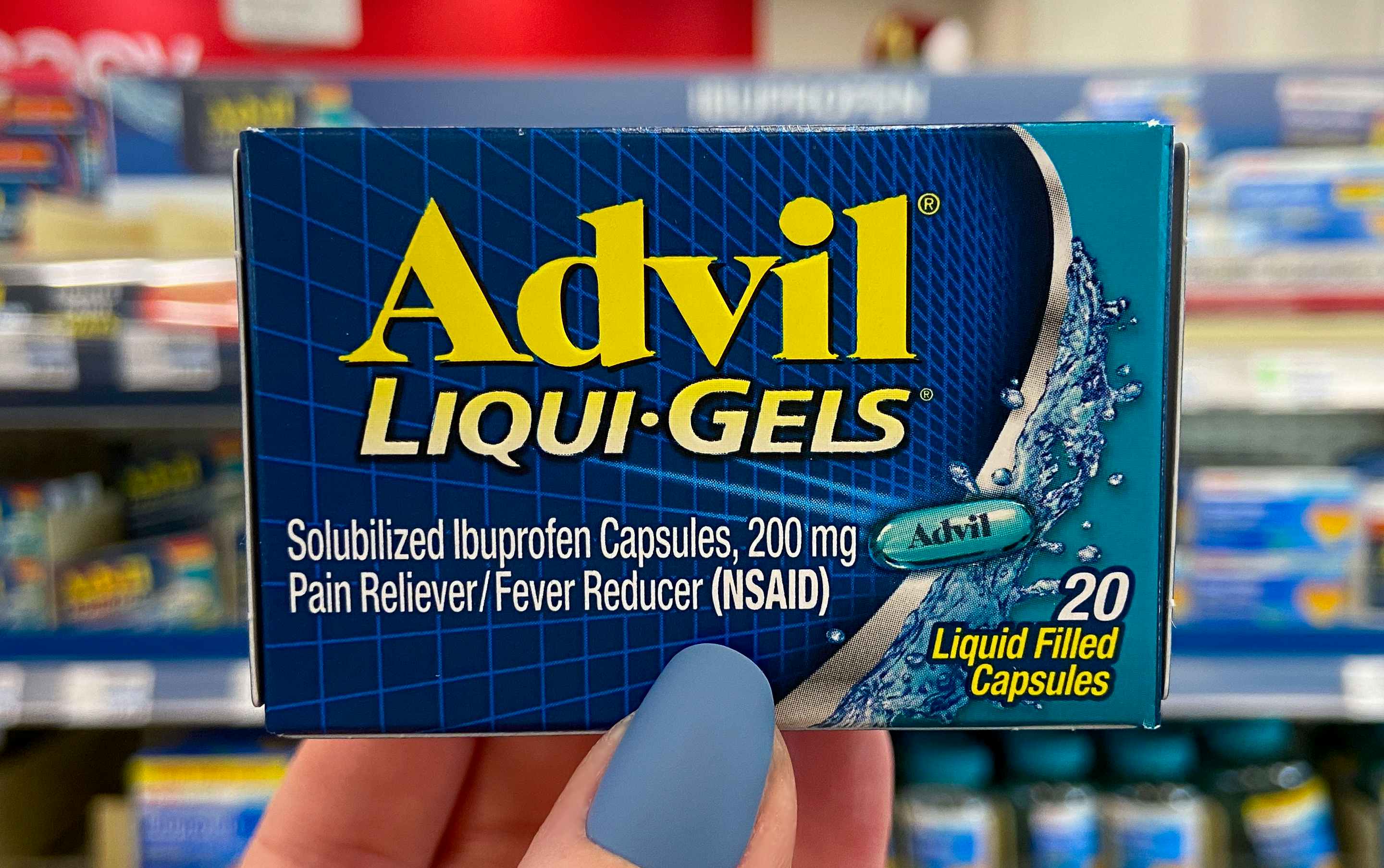 A person's hand holding up a box of advil liquid gels in store.