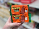 A person's hand holding two Reese's peanut butter tree chocolate treats.