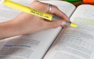 a hand using a yellow highlighter in a book
