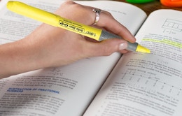 a hand using a yellow highlighter in a book
