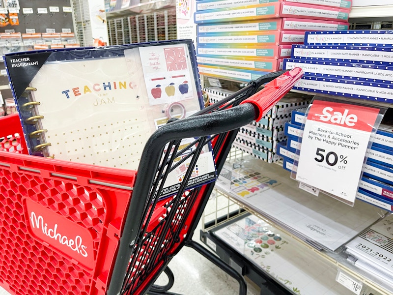 A The Happy Planner teachers planner box kit in a Michaels cart next to a shelf of more box kits on sale for 50% off at Michaels.