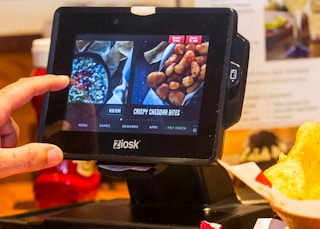 A person's hand reaching to use the Ziosk tablet on a table at Chili's.