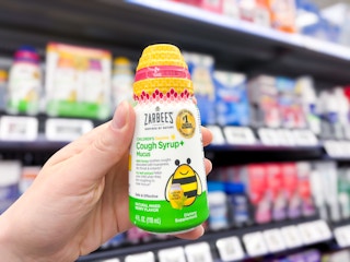 hand holding a bottle of zarbees cough syrup in walmart aisle