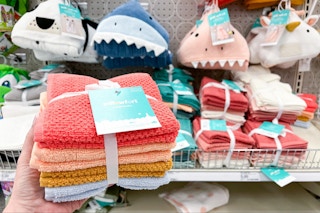 hand holding a pillowfort washcloth set in front of hooded towels at target