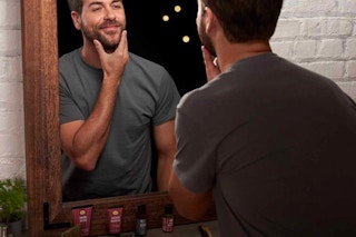 a man looking in a mirror with a shaving kit on the bathroom counter