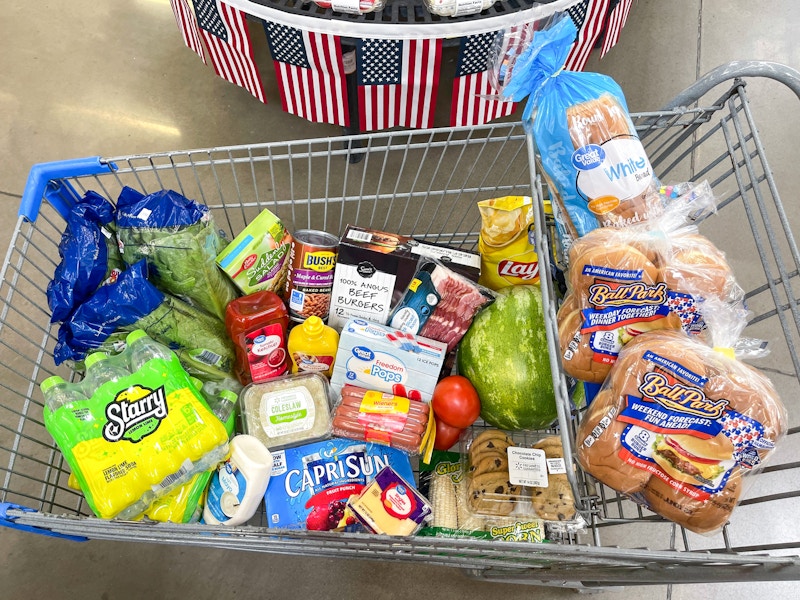 A cart filled with grilling essentials parked in front of some americana decor at Walmart