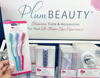 hand holding pack of Plum Beauty eyebrow shaping razors in front of display